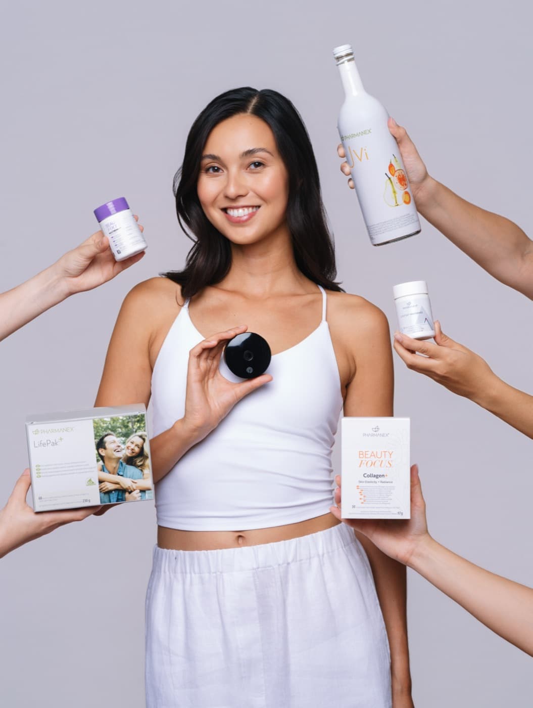 A smiling woman holding the Prysm iO scanner, surrounded by hands offering the Pharmanex LifePak, JVi and Beauty Focus products